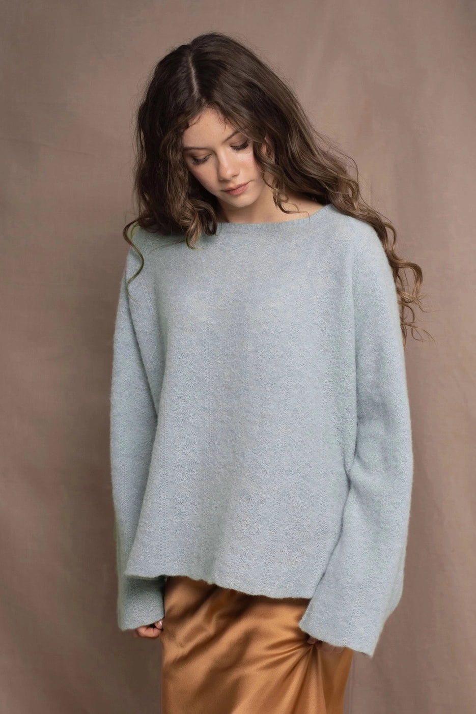 A woman wears a cashmere sweater jumper in pale blue aquamarine with a bronze silk skirt from Ireland