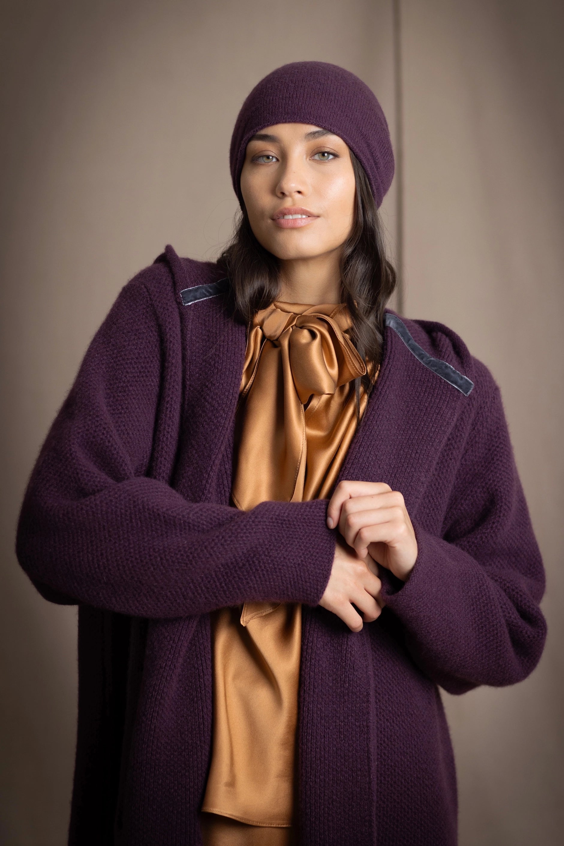 Woman wearing a purple cashmere cardigan coat and matching purple cashmere beanie hat with a bronze silk top