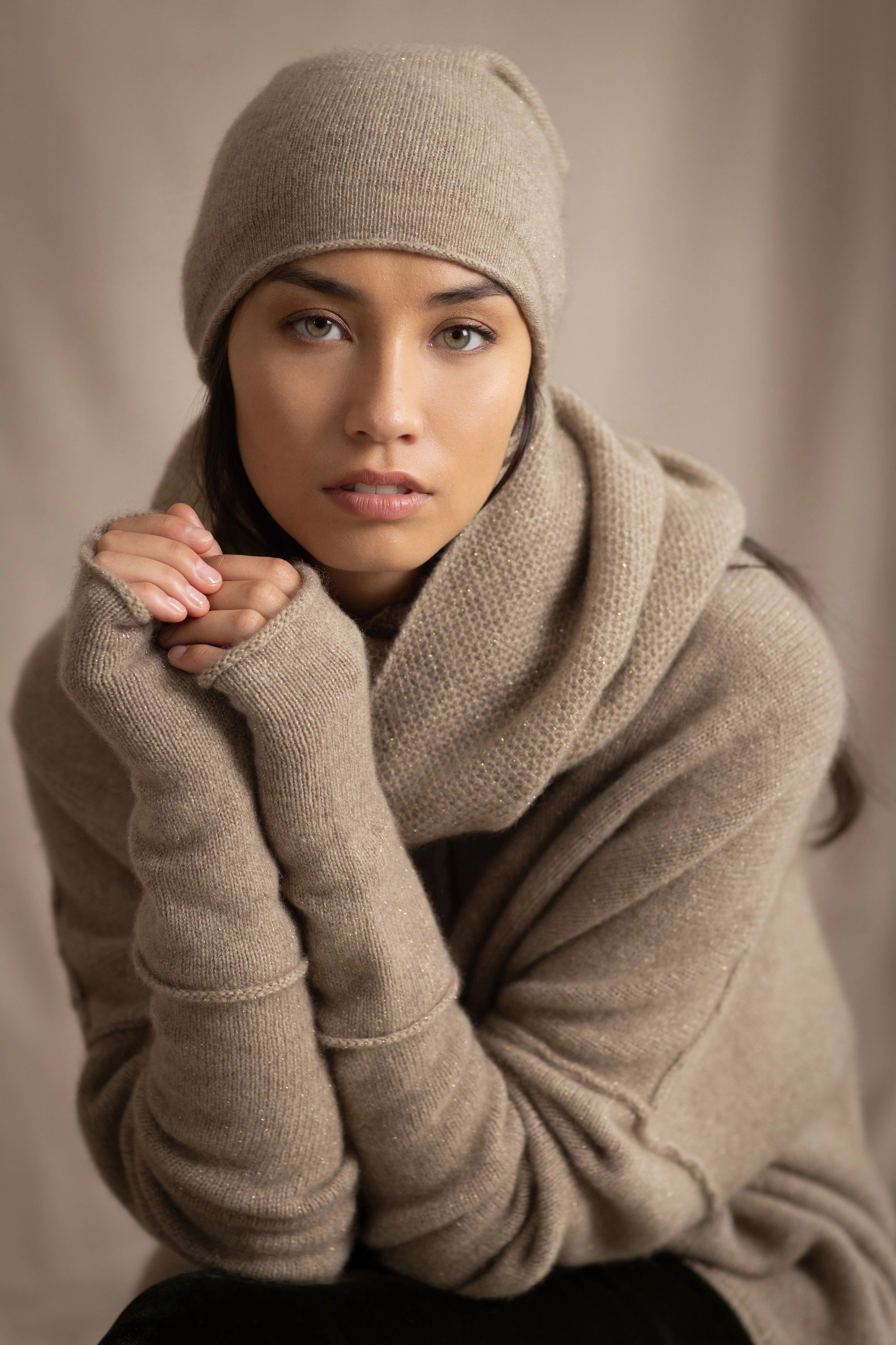 Woman wearing a beige sparkly cashmere hat, gloves, snood scarf and sweater