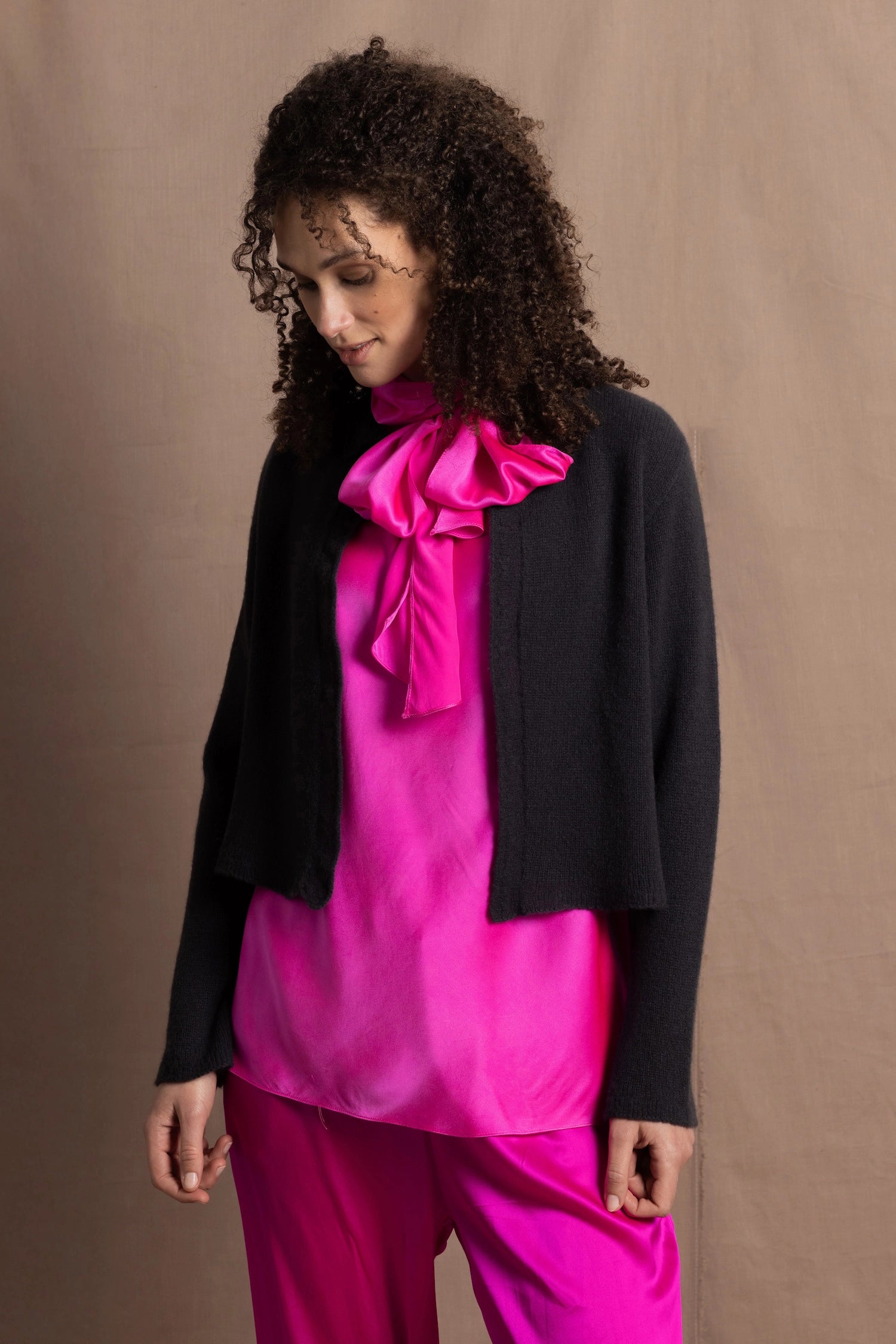 a woman wears a cashmere cardigan over silk clothing in bright pink