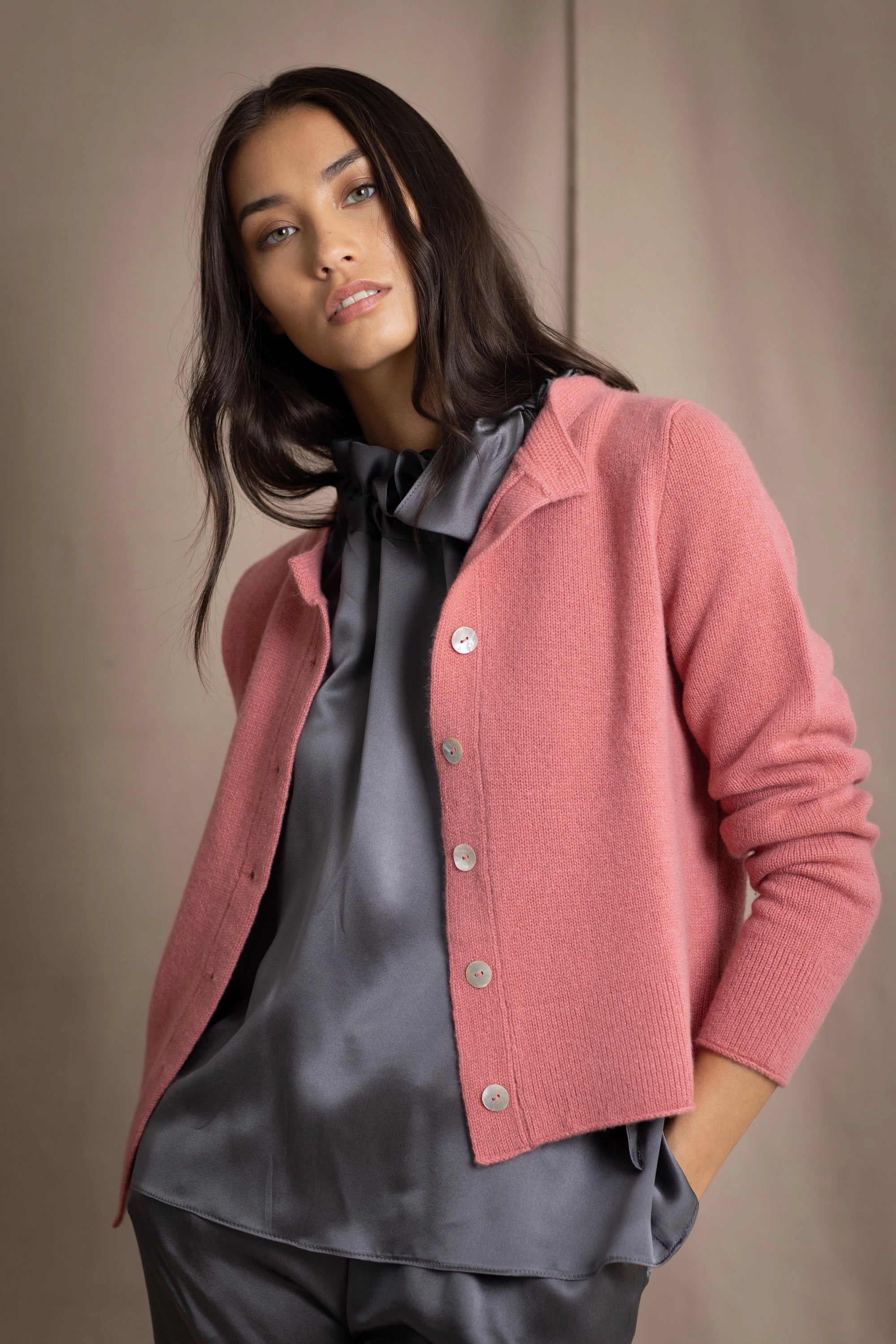 woman wearing a cashmere cardigan with buttons in dusty pink rose colour over dark grey silk top and trousers