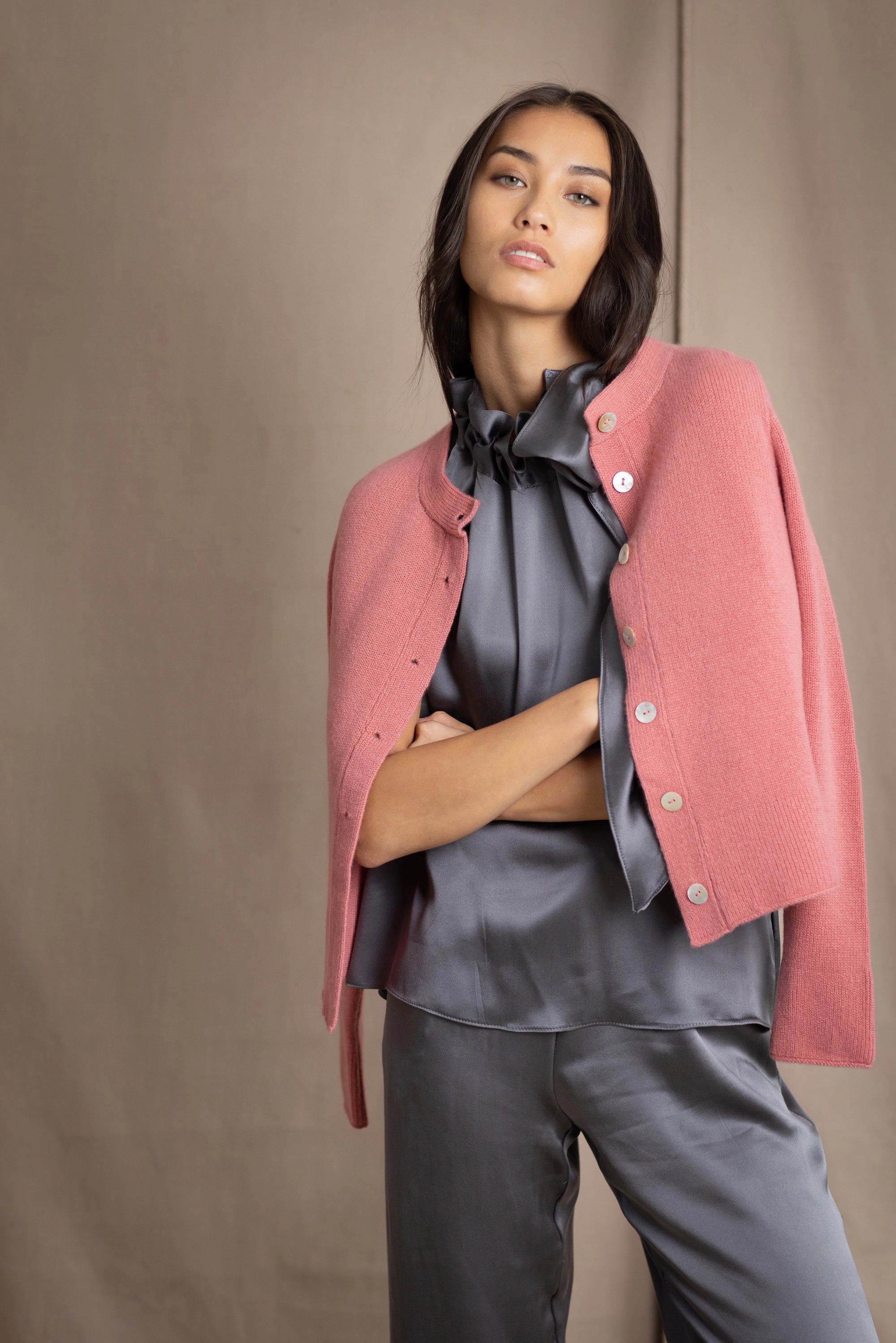 woman wearing a cashmere cardigan with buttons in dusty pink rose colour over dark grey silk top and trousers