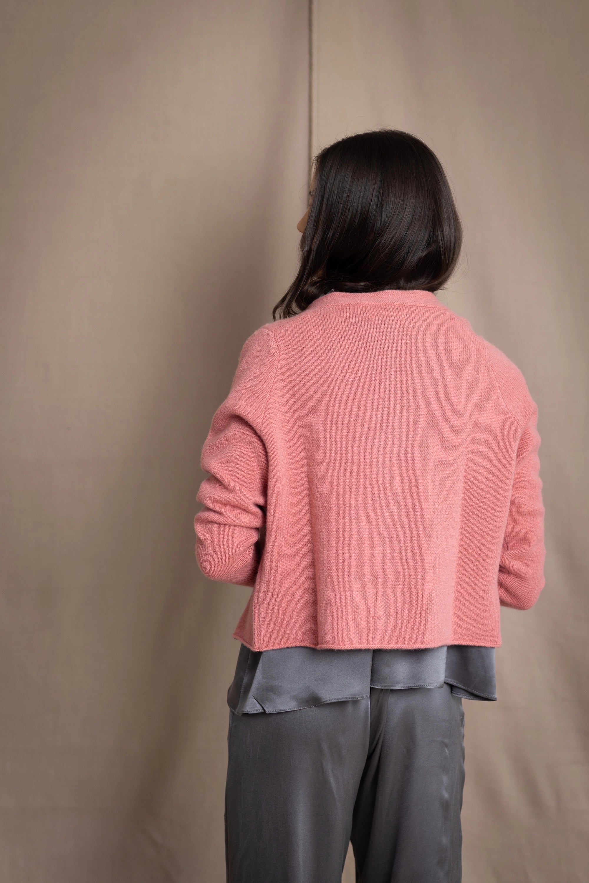 woman wearing a cashmere cardigan  in dusty pink rose with mother of pearl buttons over dark grey silk top and trousers