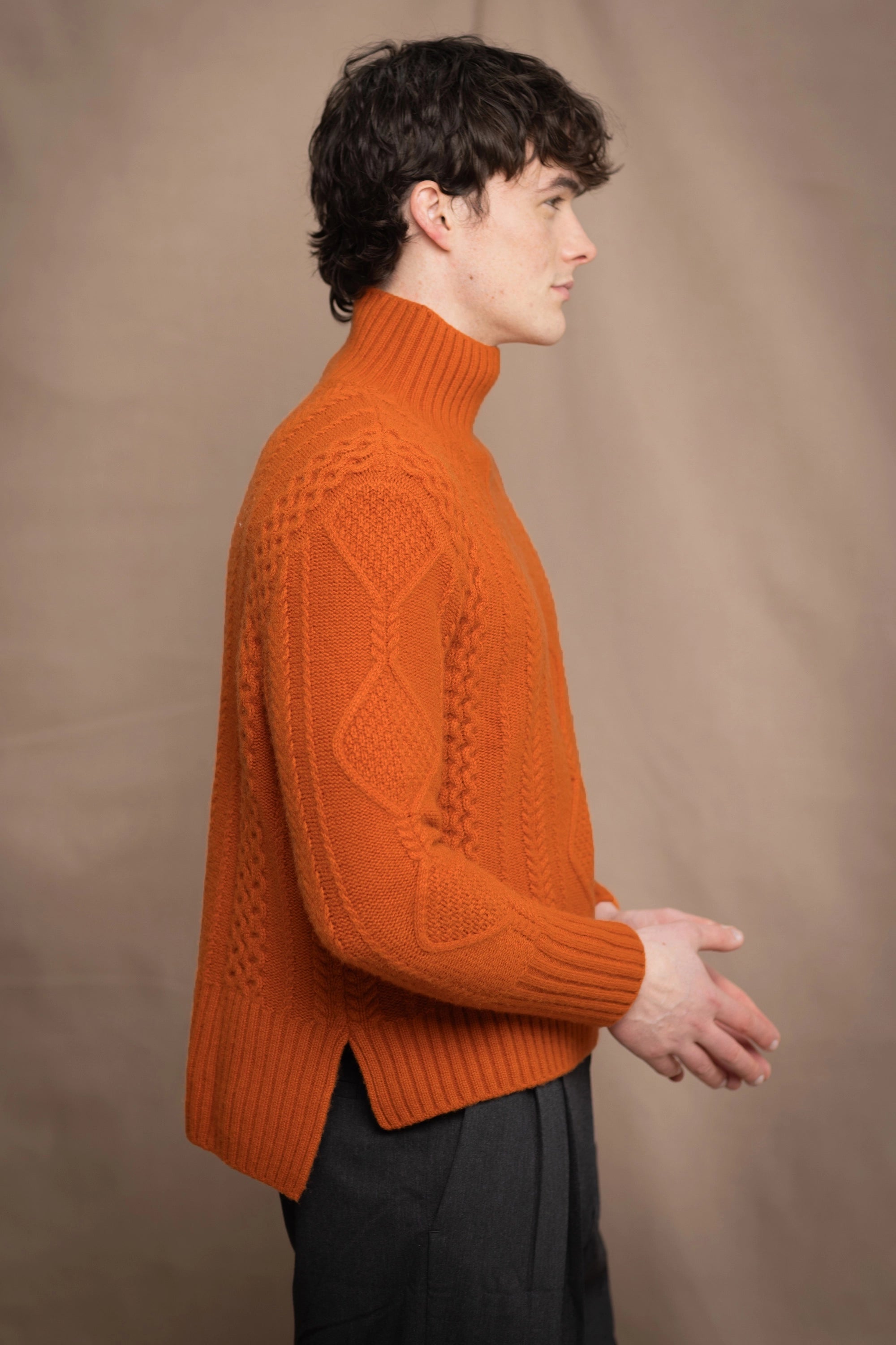 a man wearing a dark orange knitted cashmere aran sweater with cable knit Irish pattern