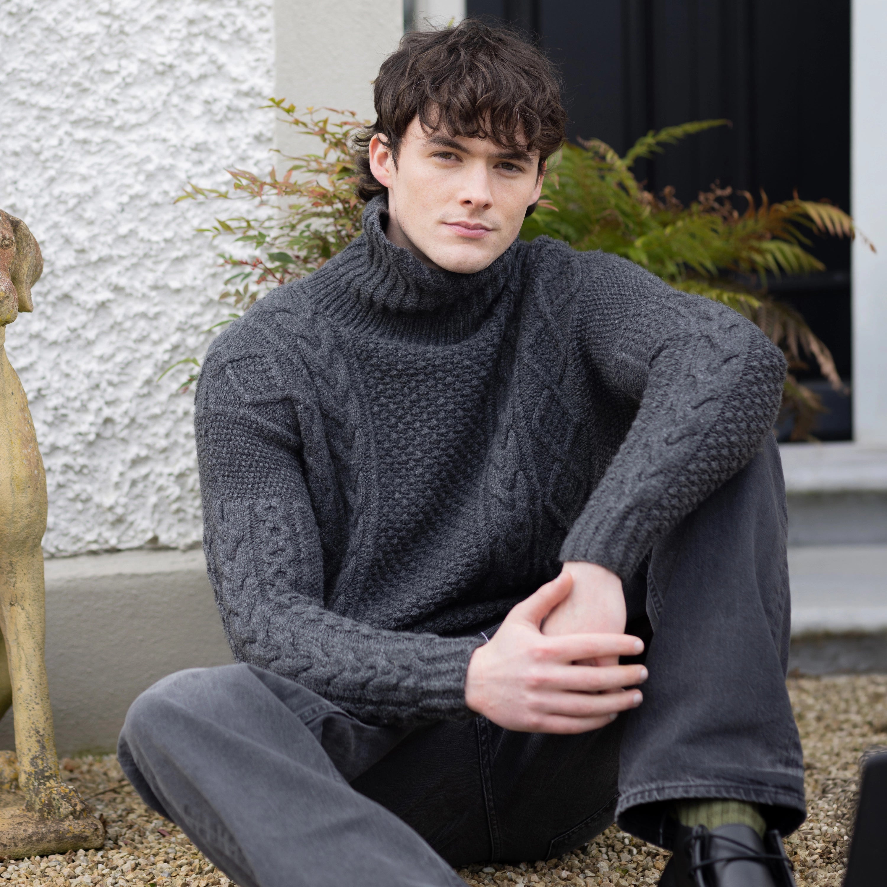 A man wearing a dark gray cable-knit  cashmere aran turtleneck sweater 