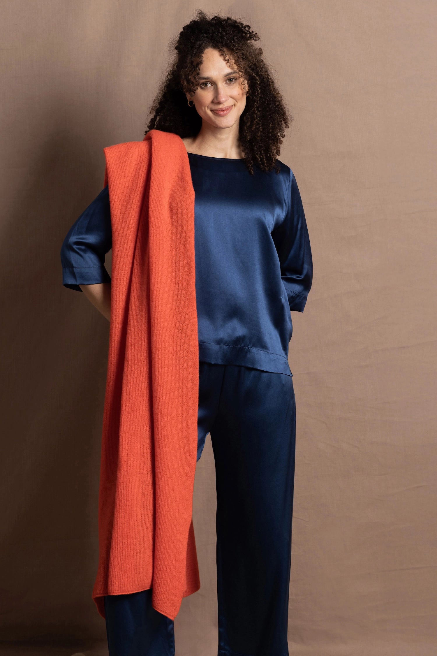 A lady wears a pure silk 3/4 sleeve blouse in teal with matching trousers and large orange cashmere wrap