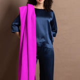 A woman wears a large neon pink cashmere wrap over her shoulder over a full teal silk to and trouser outfit