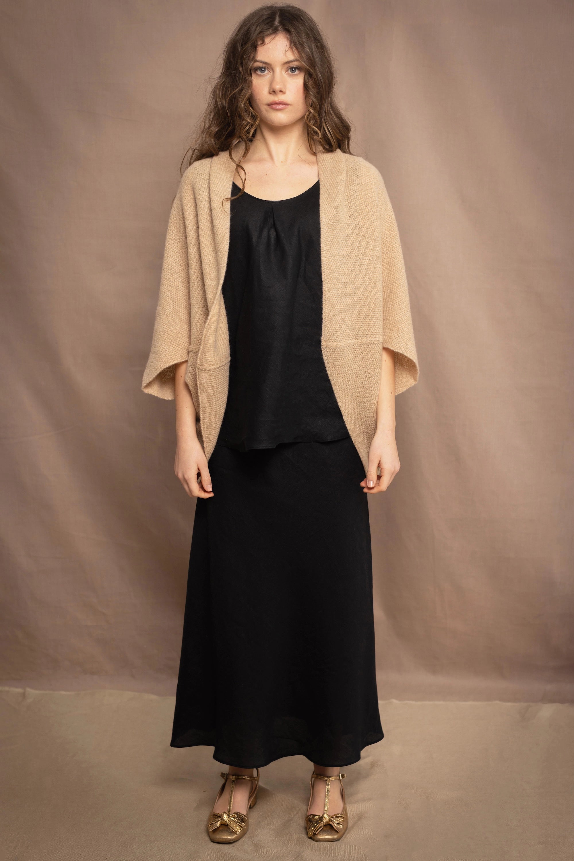 a woman wears a beige cashmere cocoon cardigan with a moss texture  over black linen top and skirt by Irish brand Madigan