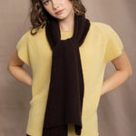a woman wears a cashmere tee in butter yellow over silk trousers in chocolate brown with a cashmere scarf in chocolate brown on top