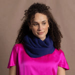 A woman wears a blue cashmere snood or infinity scarf over a bright pink silk t-shirt