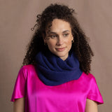 A woman wears a blue cashmere snood or infinity scarf over a bright pink silk t-shirt