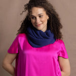 A woman wears a blue cashmere snood or infinity scarf over a bright pink silk t-shirt