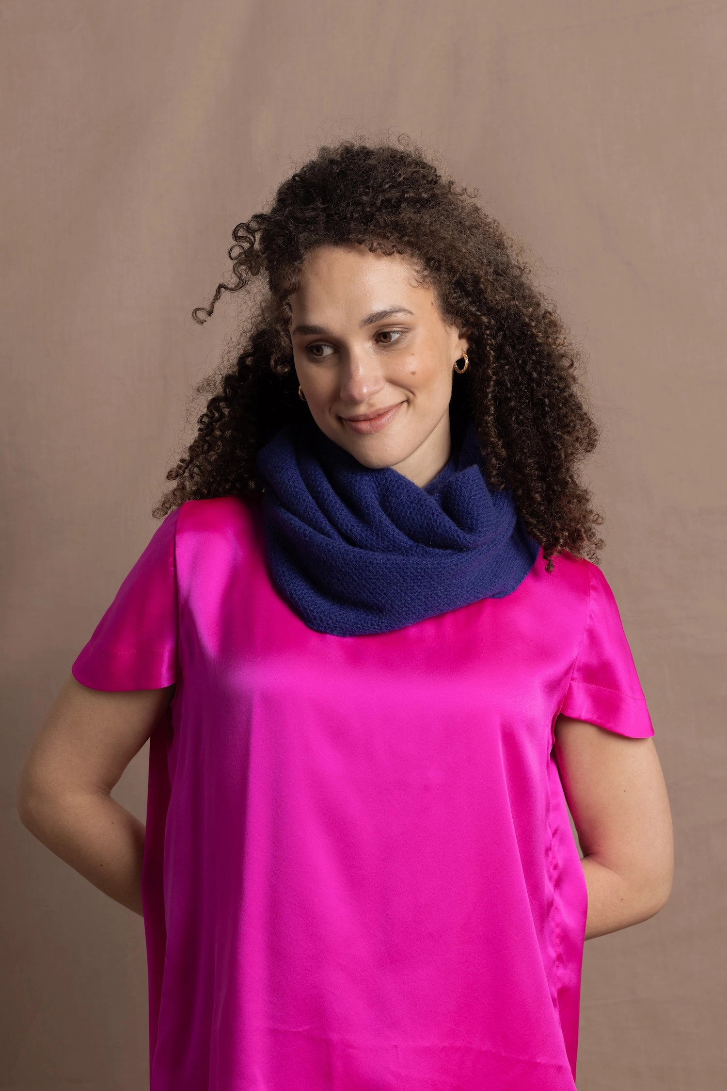 A woman wears a blue cashmere snood or infinity scarf over a bright pink silk t-shirt