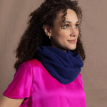 A woman wears a blue cashmere snood or infinity scarf over a bright pink silk t-shirt