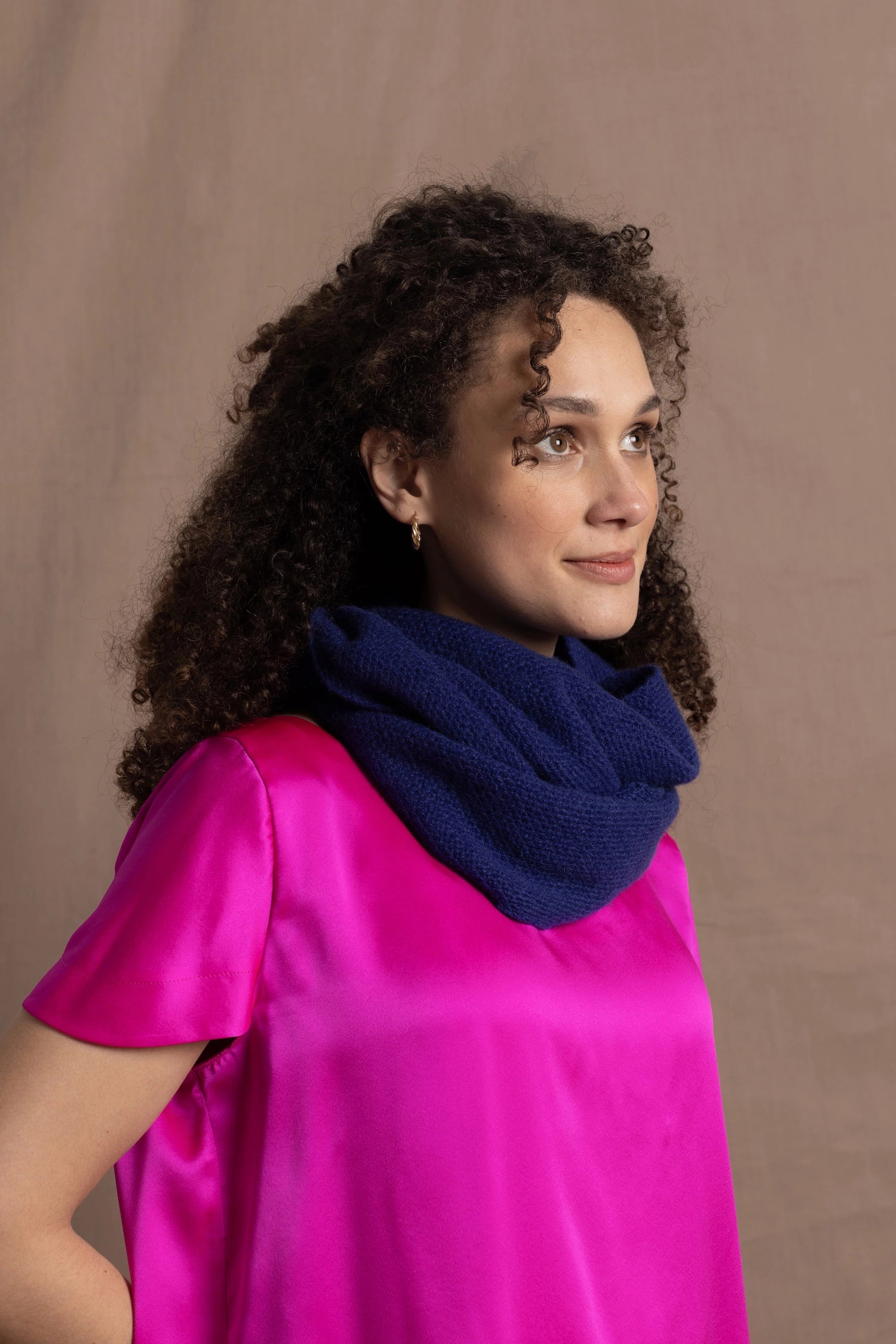 A woman wears a blue cashmere snood or infinity scarf over a bright pink silk t-shirt