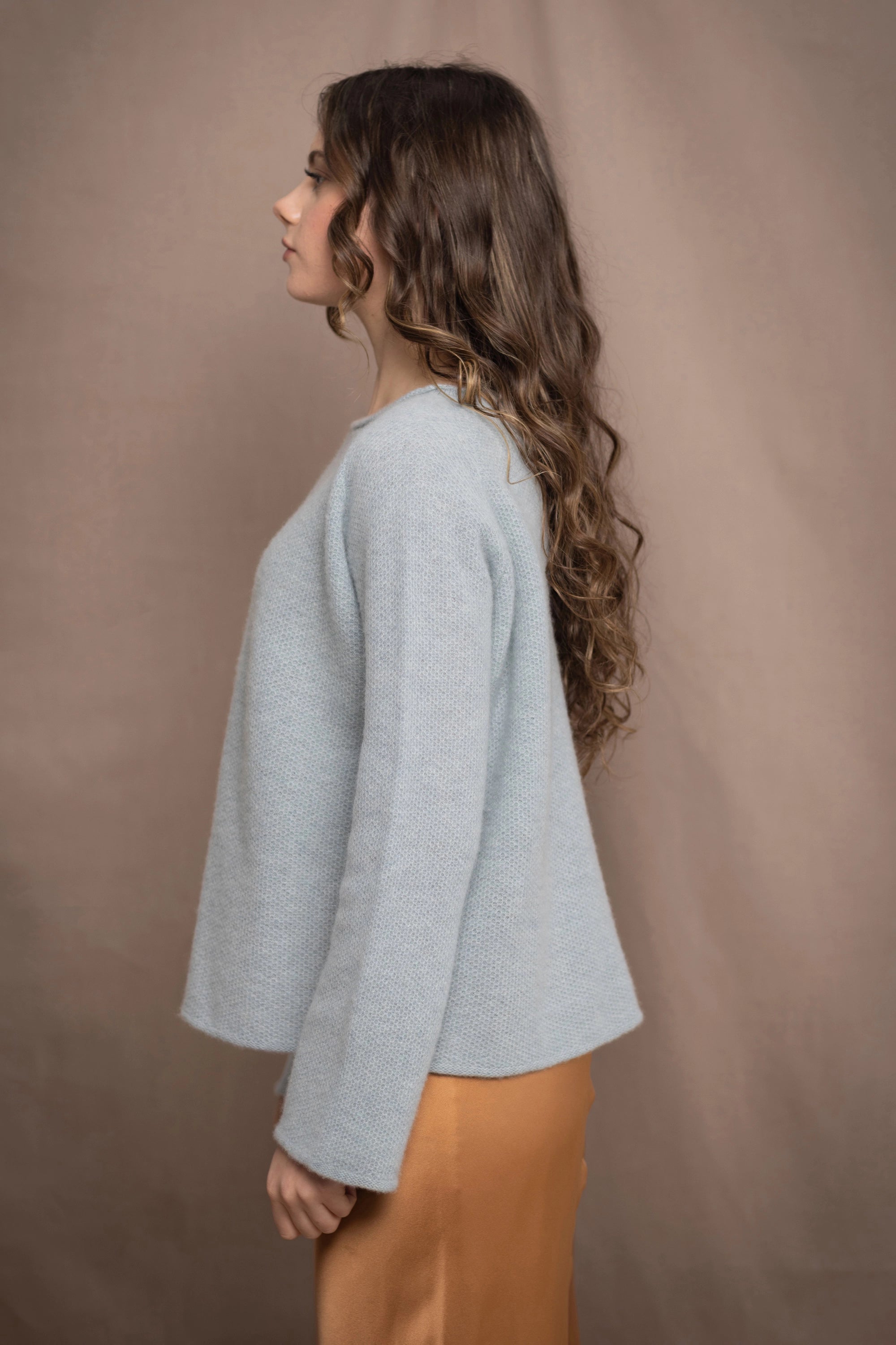 a woman wearing a light blue pure cashmere raglan sleeve sweater jumper over silk skirt in bronze