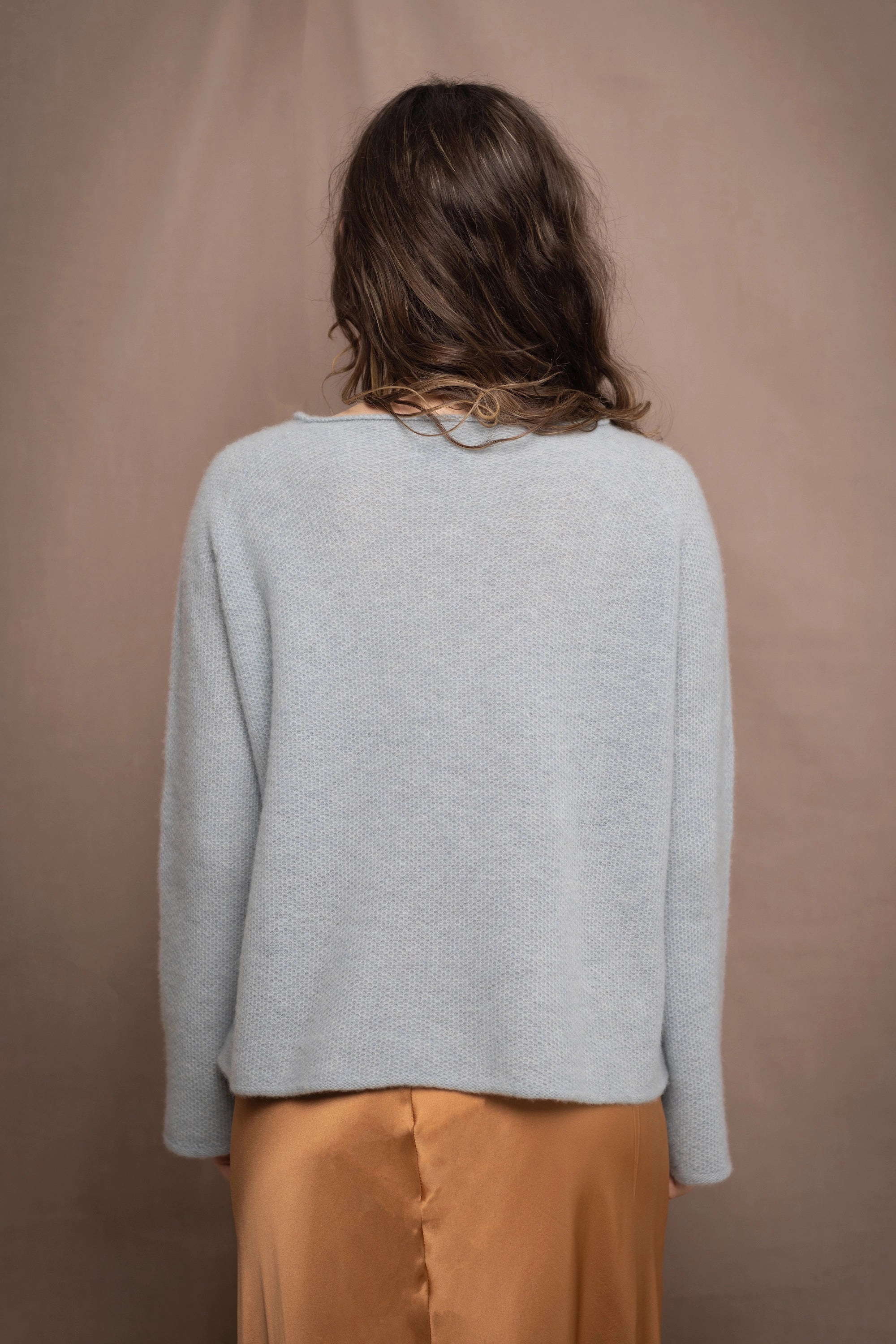 a woman wearing a light blue pure cashmere raglan sleeve sweater jumper over silk skirt in bronze