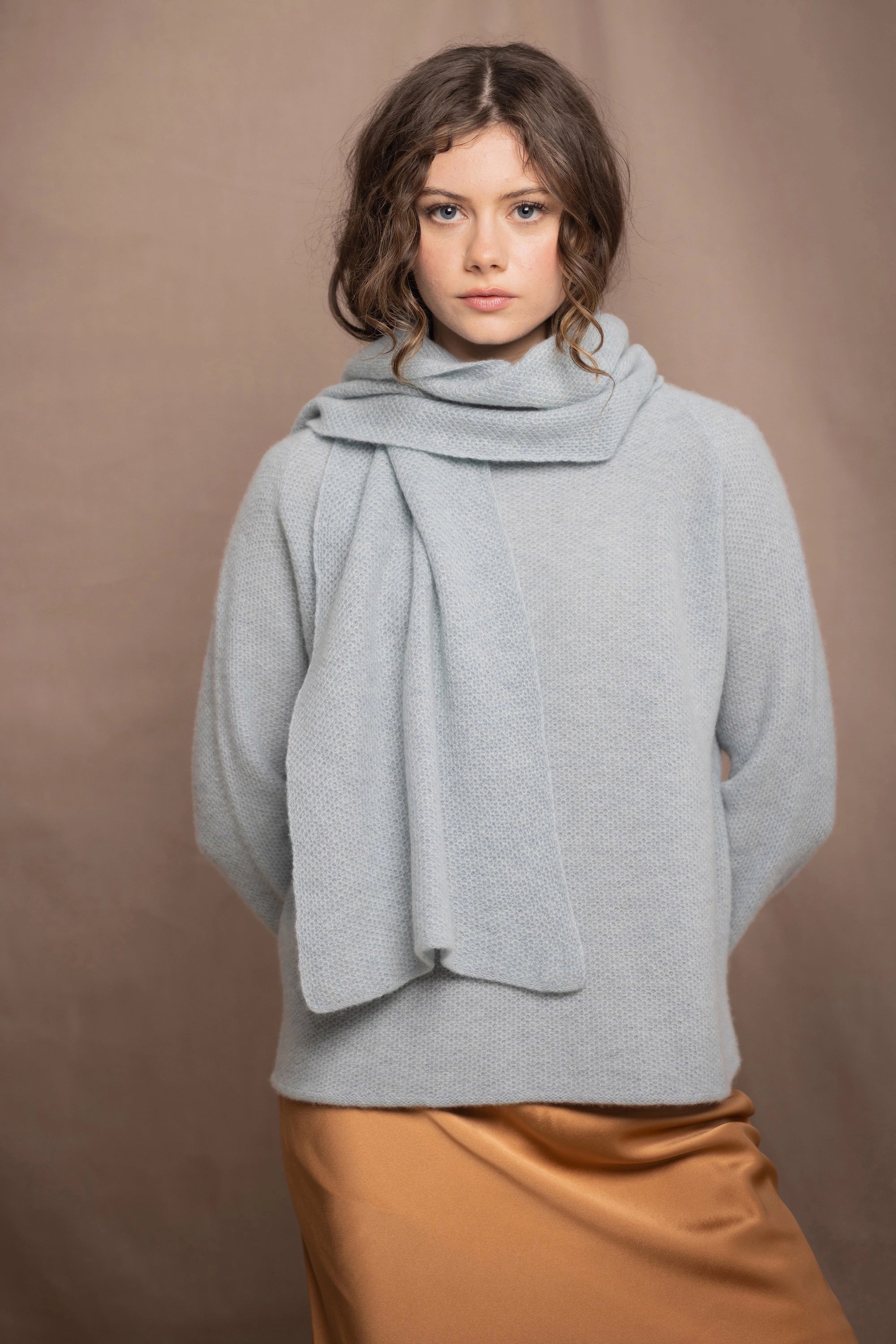 a woman wearing a light blue pure cashmere raglan sleeve sweater jumper and matching cashmere scarf over silk skirt in bronze