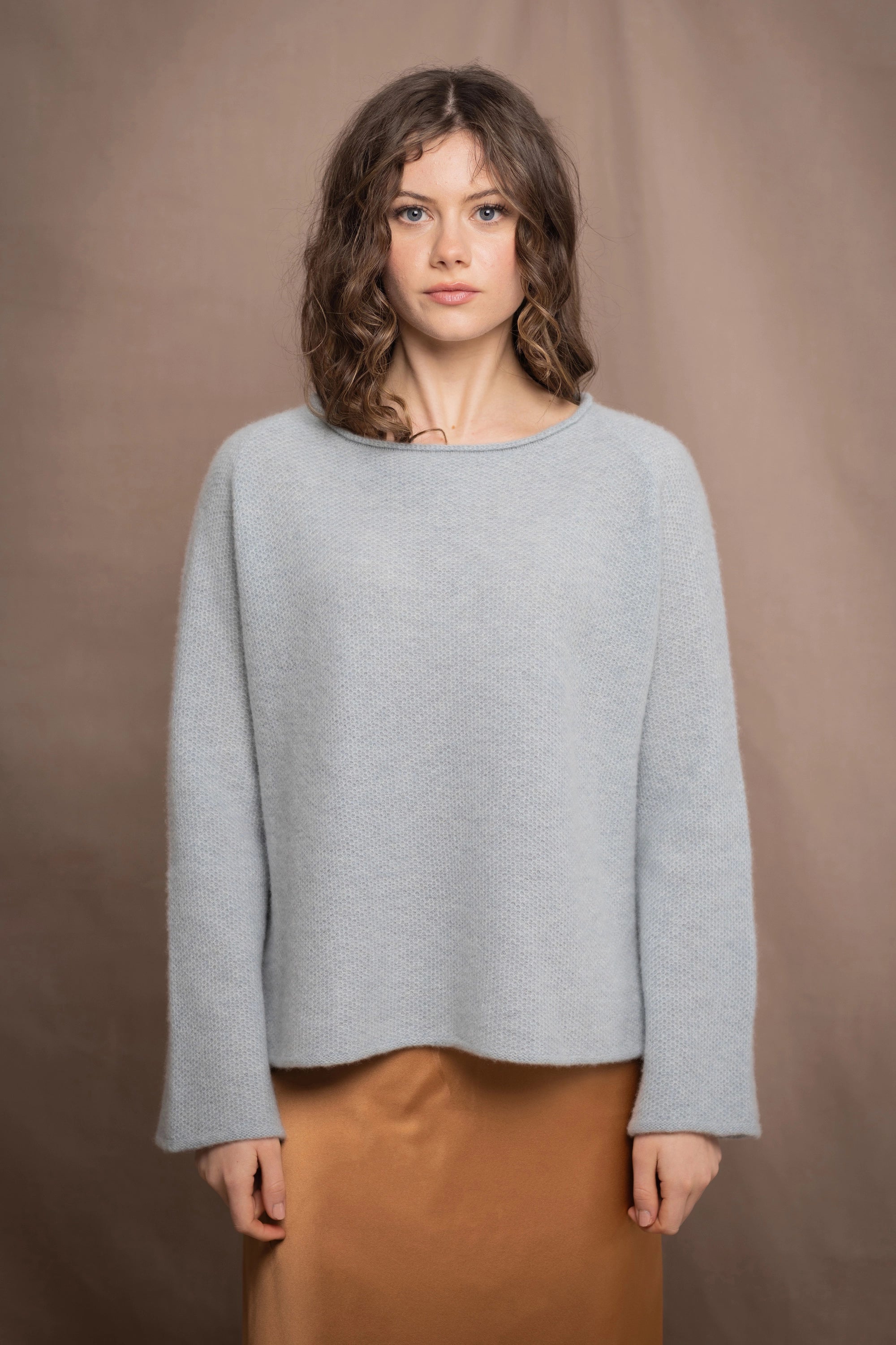 a woman wearing a light blue pure cashmere raglan sleeve sweater jumper over silk skirt in bronze