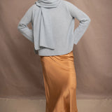 a woman wearing a light blue pure cashmere raglan sleeve sweater jumper and matching cashmere scarf over silk skirt in bronze