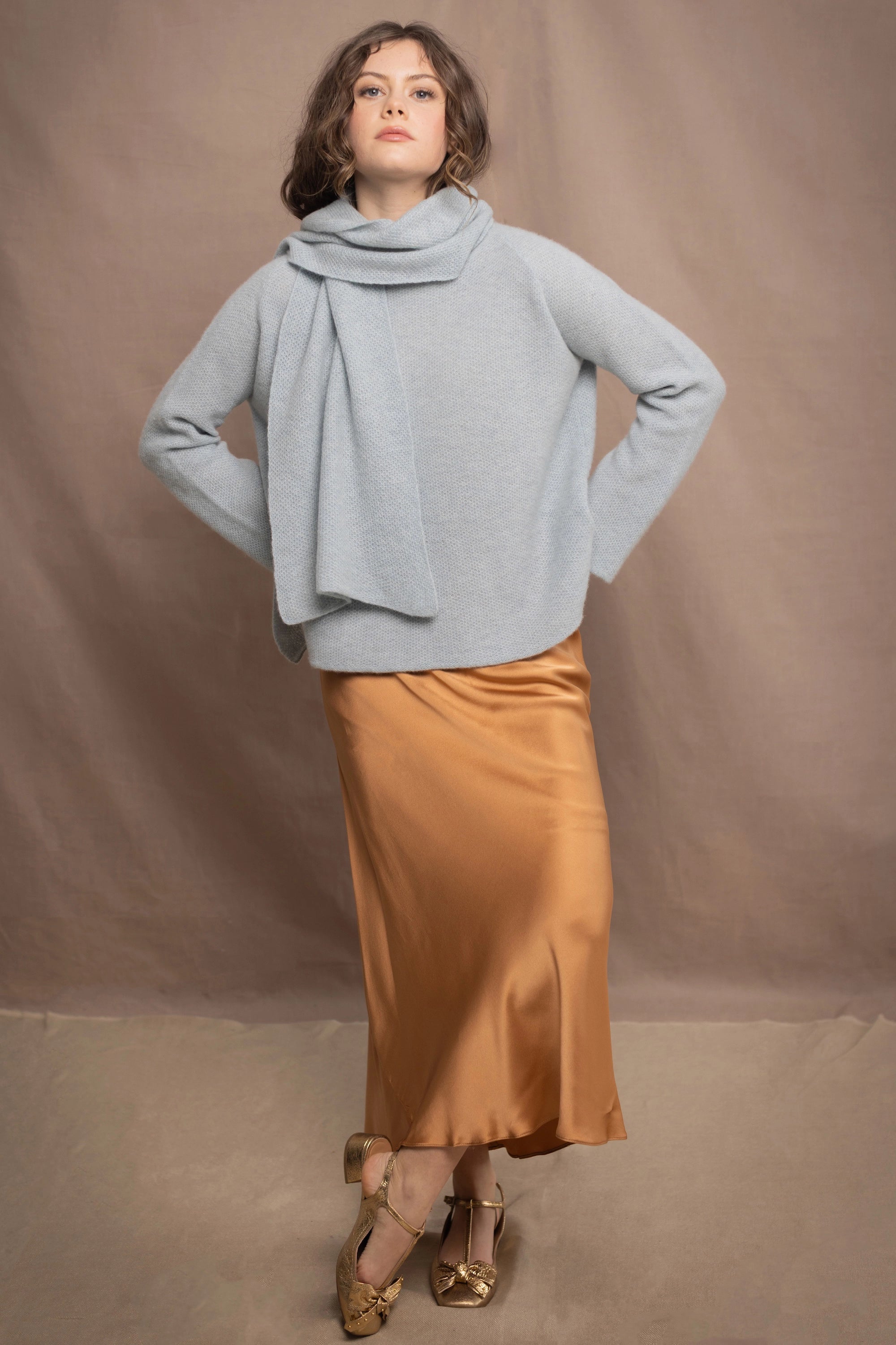 a woman wearing a light blue pure cashmere raglan sleeve sweater jumper and matching cashmere scarf over silk skirt in bronze
