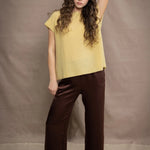 a woman wears a cashmere tee in butter yellow over silk trousers in chocolate brown 