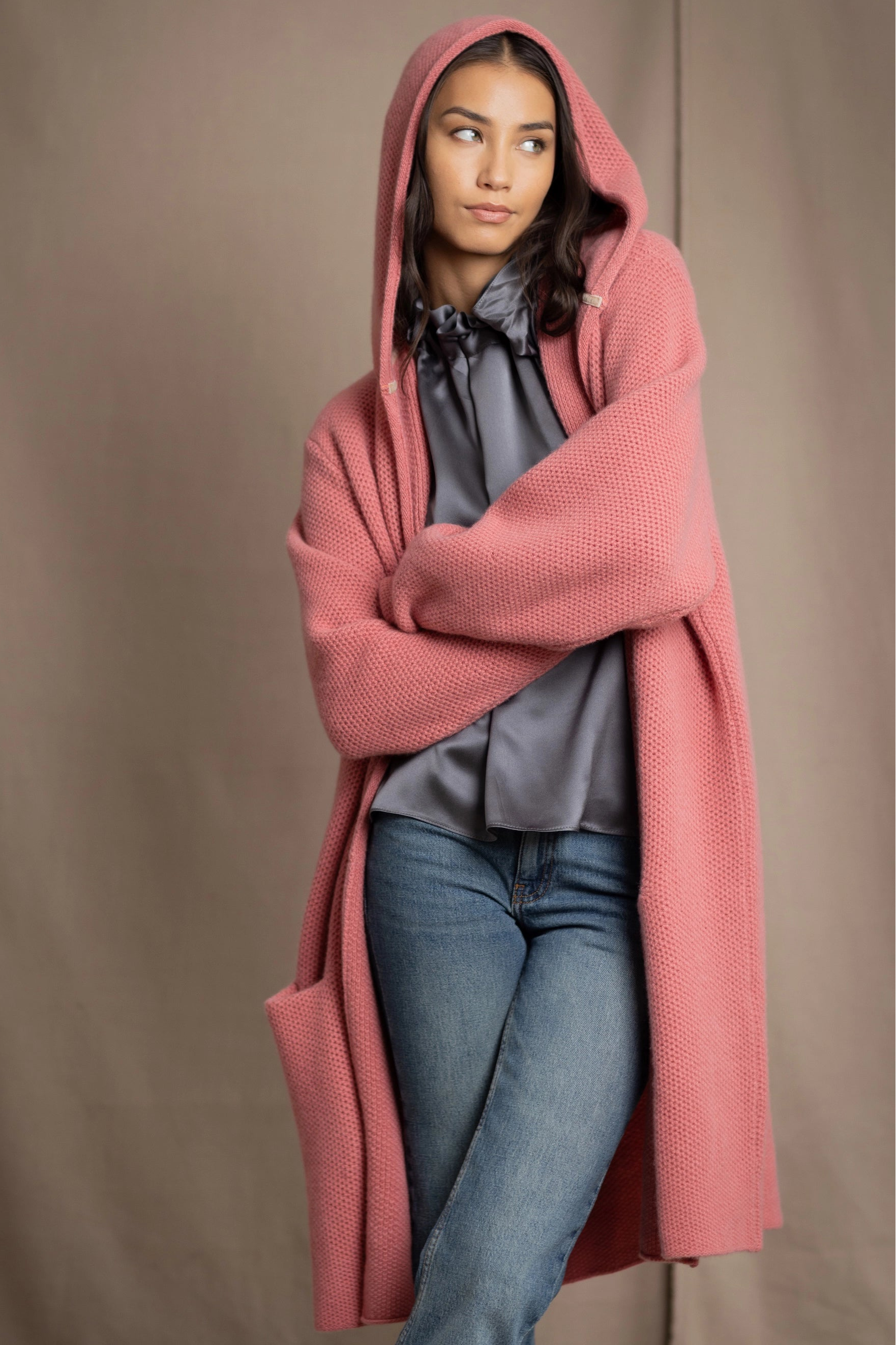 Woman wearing a long cashmere coat in dusty rose pink over a  pewter gray silk top and blue jeans