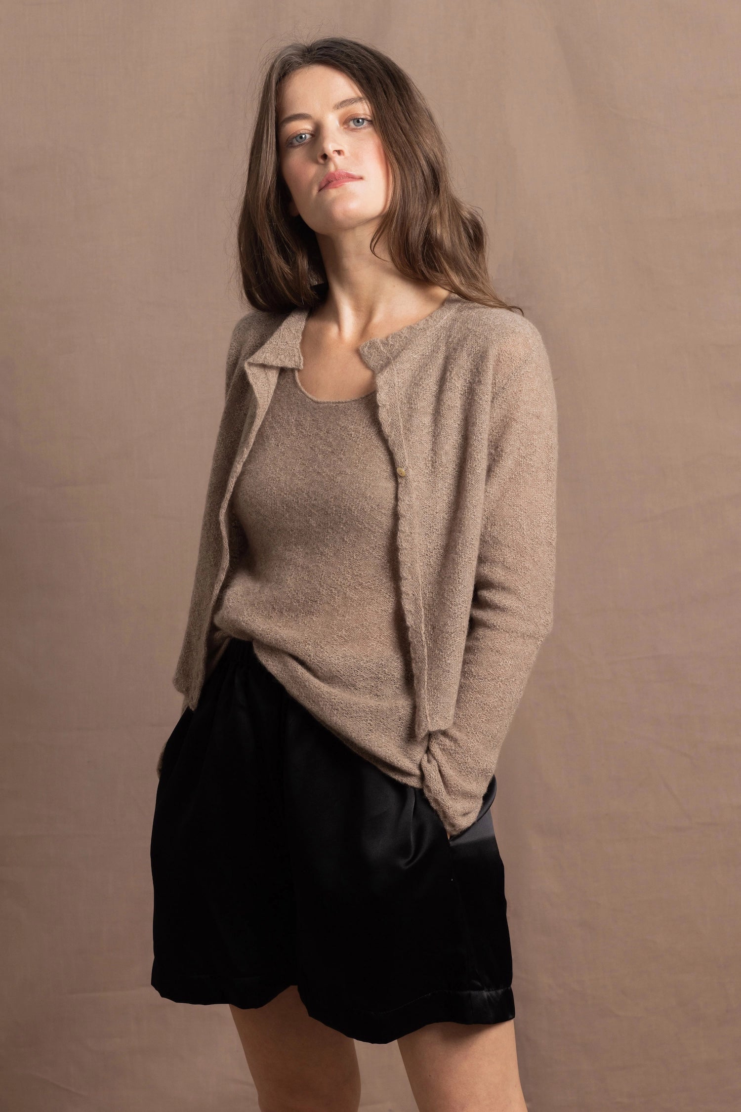 A woman wears a pure cashmere twinset cardigan with matching vest top in Beige with silk shorts in black
