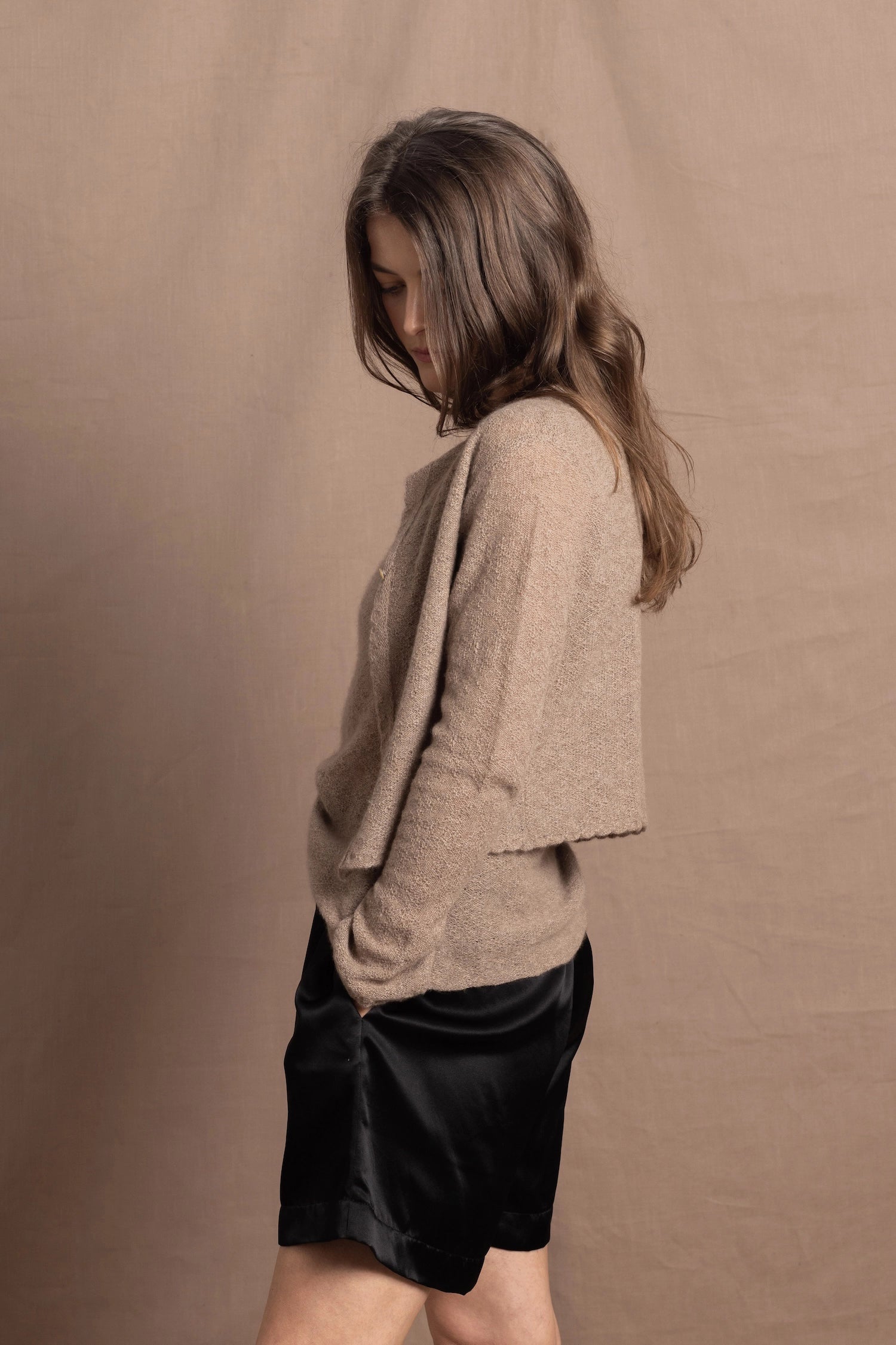 A woman wears a pure cashmere twinset cardigan with matching vest top in Beige with silk shorts in black