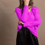 A woman wears a cashmere vest top and matching cardigan in neon pink with black silk shorts