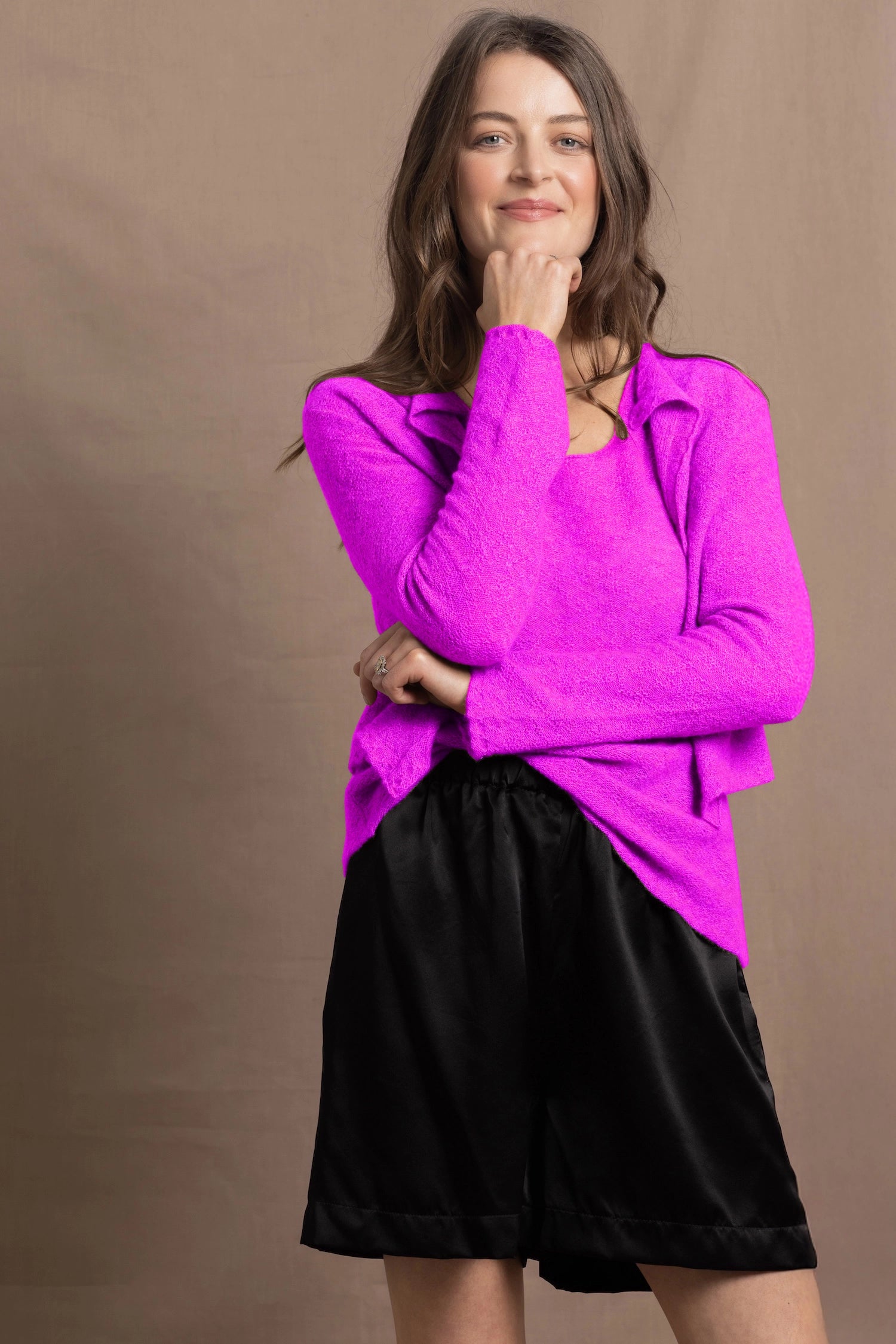 A woman wears a cashmere vest top and matching cardigan in neon pink with black silk shorts