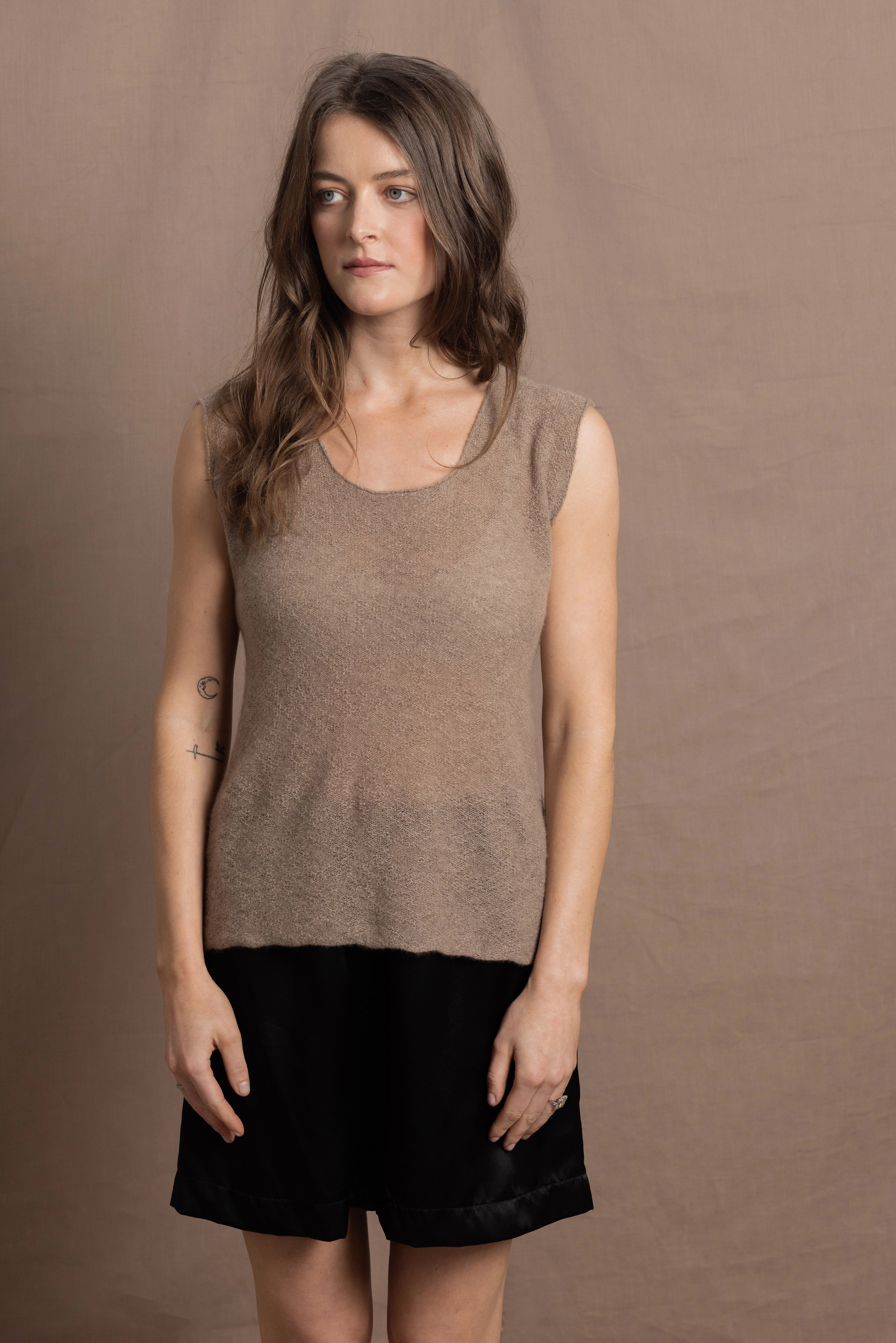A woman wears a 100% pure cashmere sleeveless vest top in beige with black silk shorts