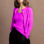A woman wears a cashmere vest top and matching cardigan in neon pink with black silk shorts