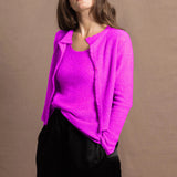 A woman wears a cashmere vest top and matching cardigan in neon pink with black silk shorts