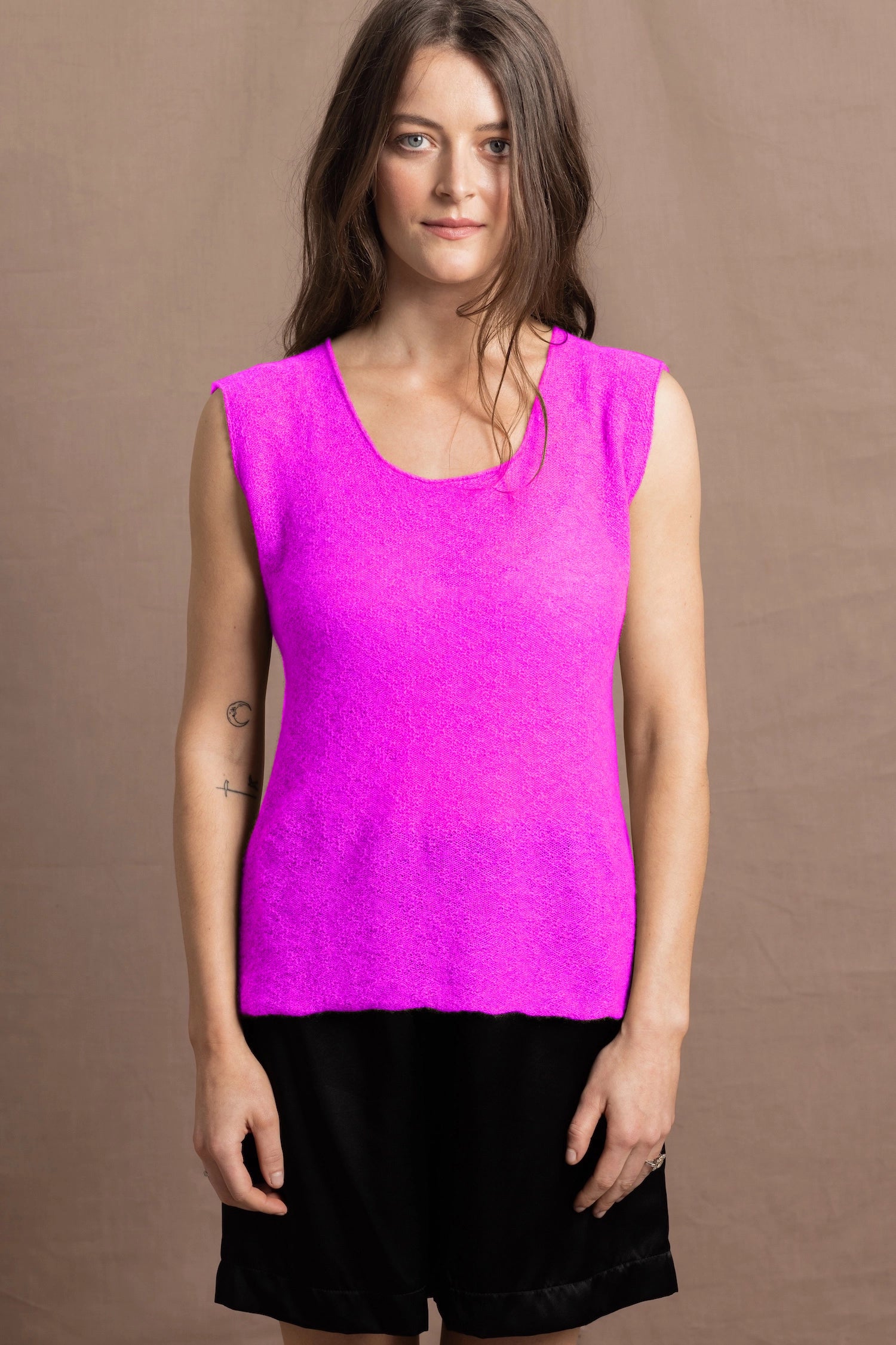 A woman wears a cashmere vest top in neon pink with black silk shorts
