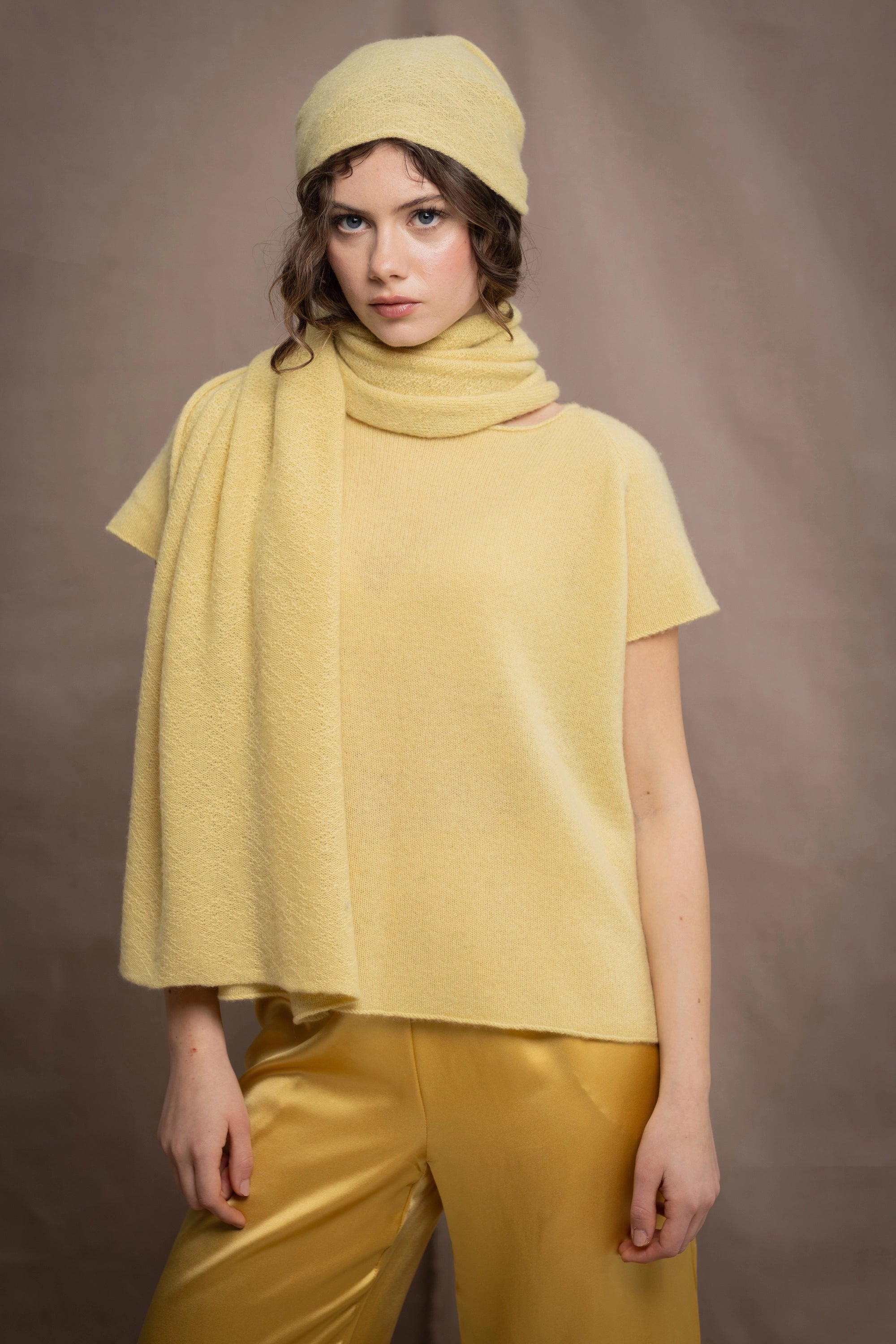 A woman wears a large cashmere scarf in pale yellow with matching cashmere beanie hat and cashmere tee sweater by Madigan Cashmere 