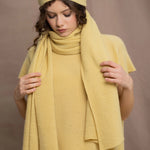 A woman wears a large cashmere scarf in pale yellow with matching cashmere beanie hat and cashmere tee sweater by Madigan Cashmere 