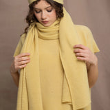 A woman wears a large cashmere scarf in pale yellow with matching cashmere beanie hat and cashmere tee sweater by Madigan Cashmere 