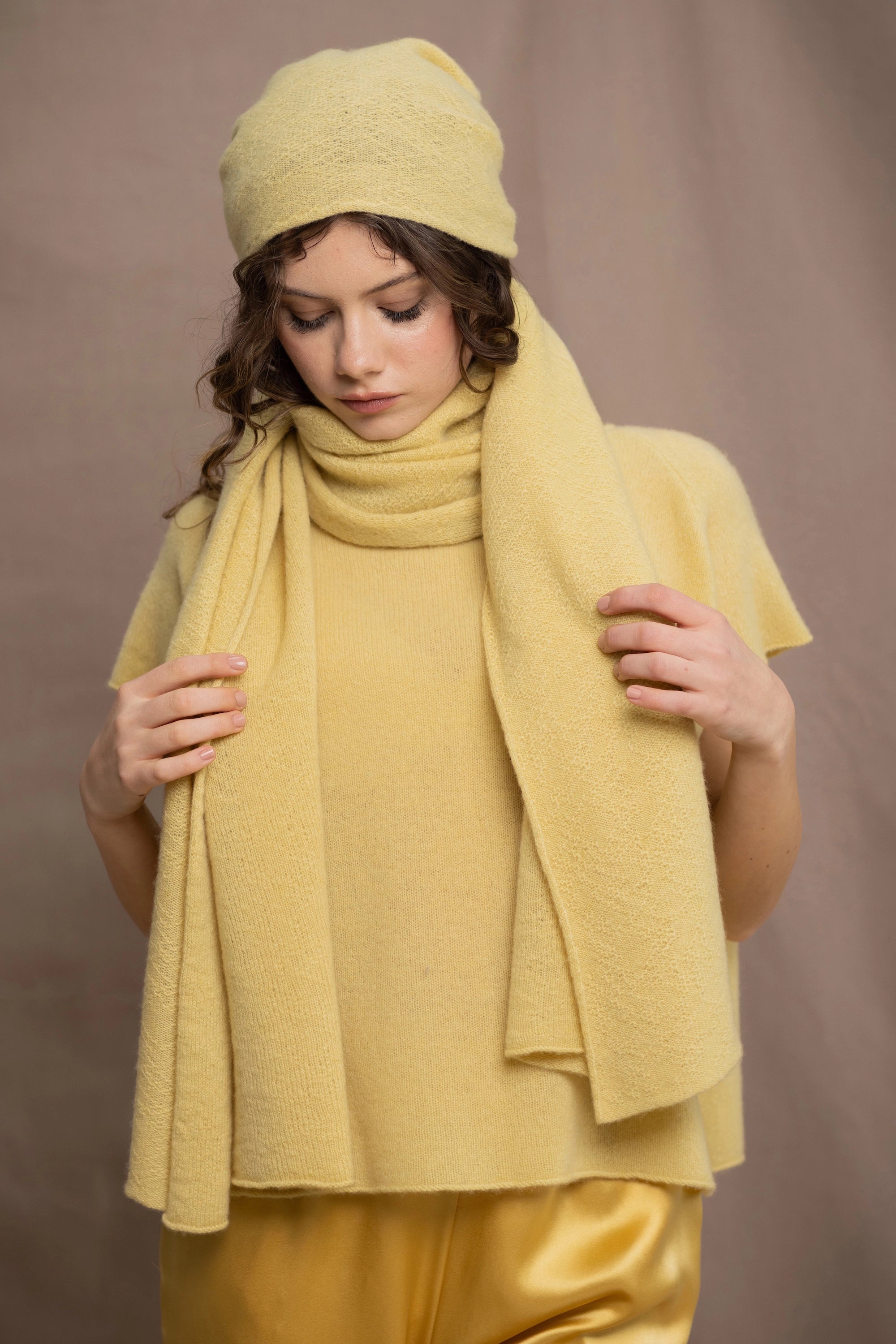 A woman wears a large cashmere scarf in pale yellow with matching cashmere beanie hat and cashmere tee sweater by Madigan Cashmere 