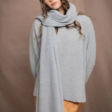 a woman wears a cashmere wrap shawl over a matching cashmere sweater and cashmere beanie in a pale blue turquoise colour