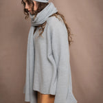 a woman wears a cashmere wrap shawl over a matching cashmere sweater and cashmere beanie in a pale blue turquoise colour