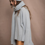 a woman wears a cashmere wrap shawl over a matching cashmere sweater and cashmere beanie in a pale blue turquoise colour