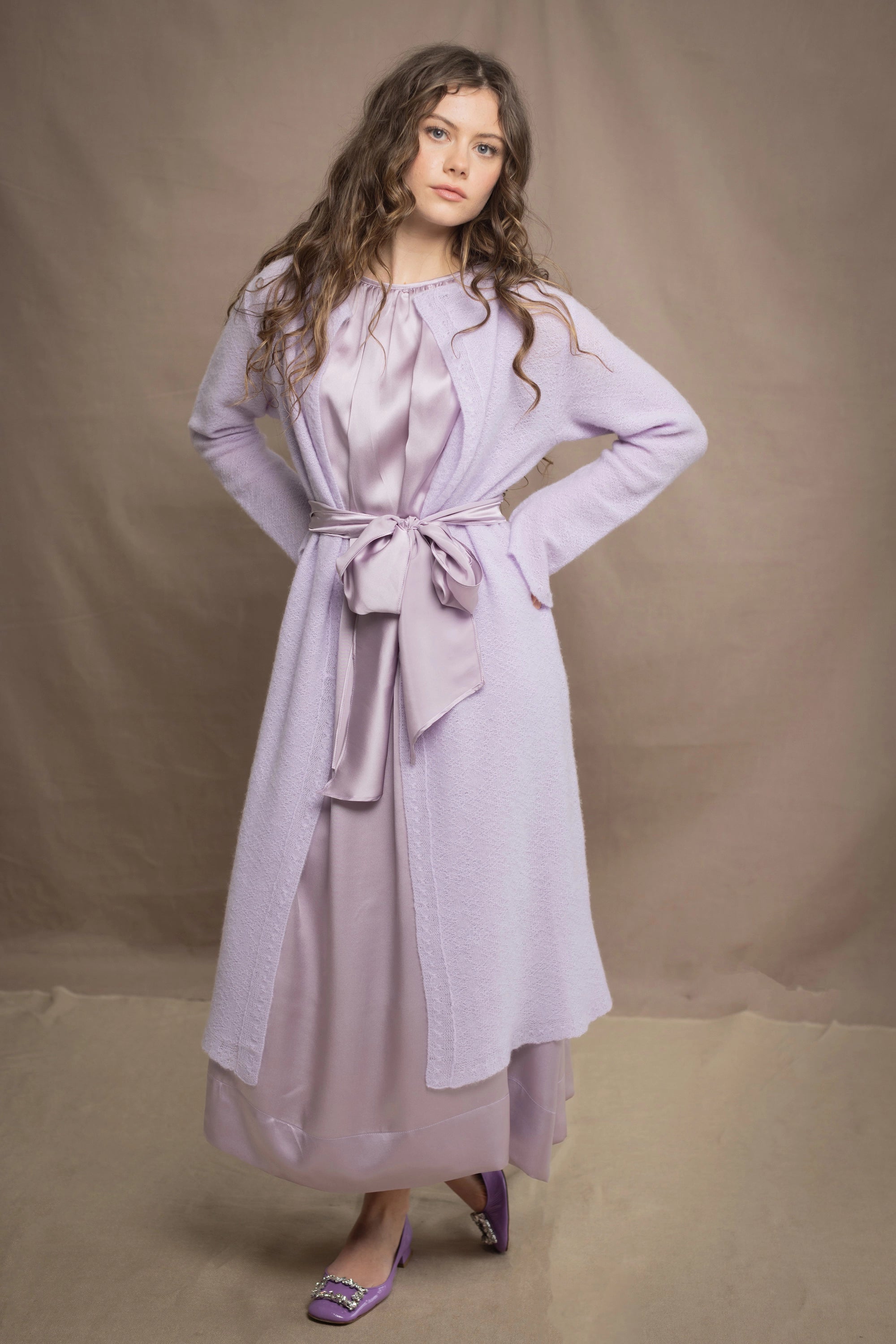 Woman wears a light purple cashmere cardigan coat over a matching silk dress by Irish brand Madigan