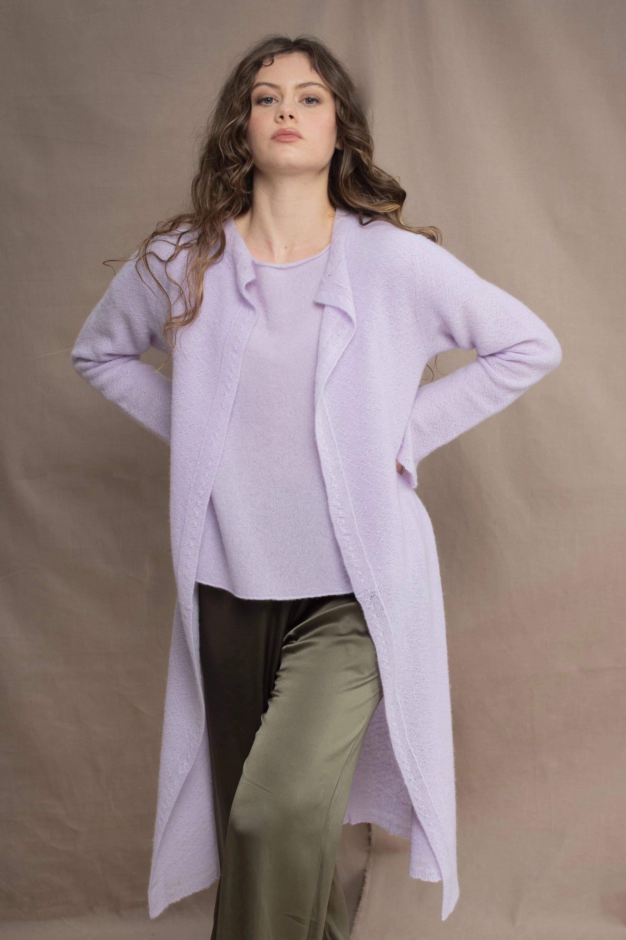 a woman wears  a 100% pure cashmere tee sweater and long cardigan coat in light purple by Irish brand Madigan Cashmere and silk trousers in dark green