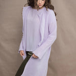 a woman wears  a 100% pure cashmere tee sweater and long cardigan coat in light purple by Irish brand Madigan Cashmere and silk trousers in dark green