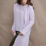 a woman wears  a 100% pure cashmere tee sweater and long cardigan coat in light purple by Irish brand Madigan Cashmere and silk trousers in dark green
