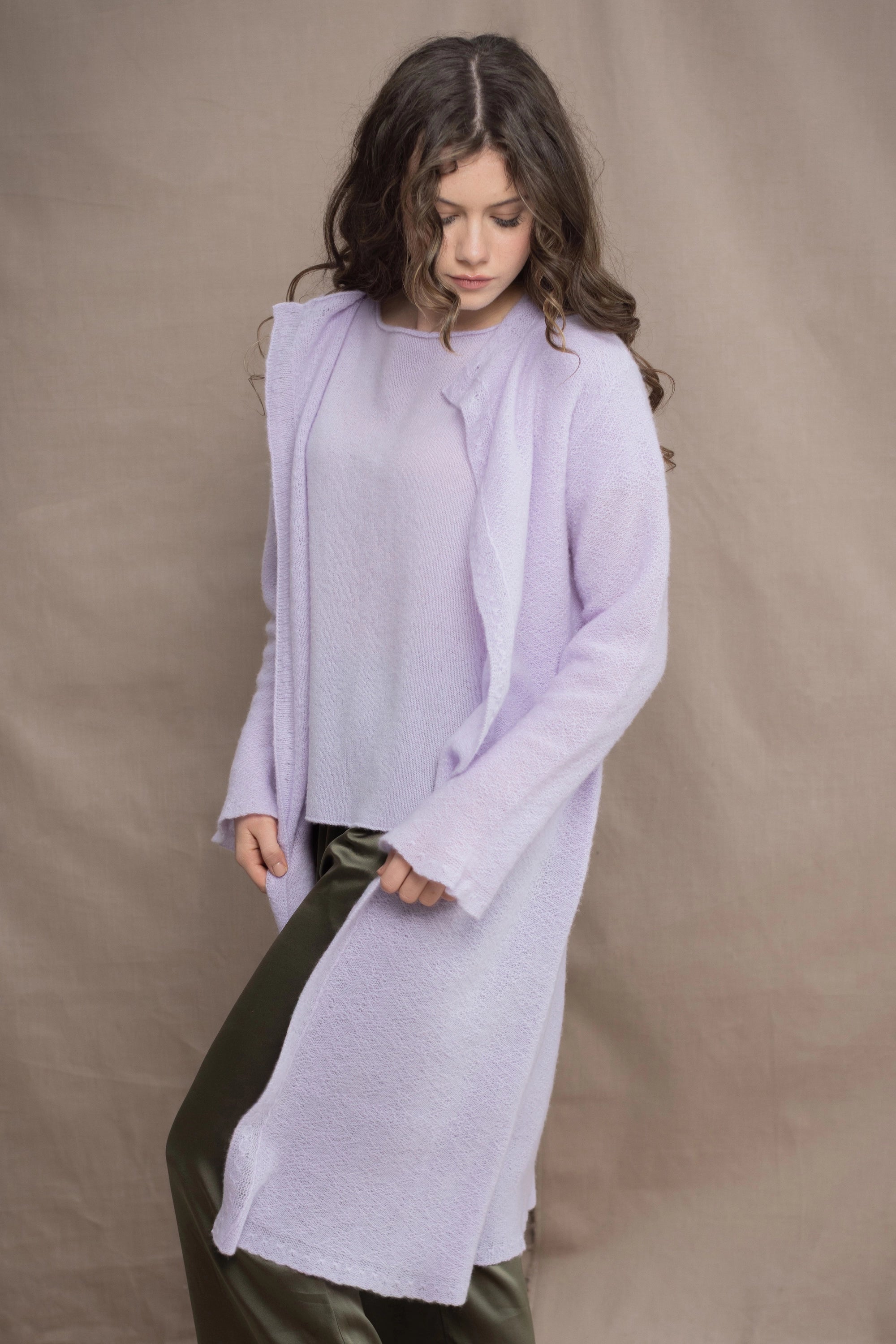a woman wears  a 100% pure cashmere tee sweater and long cardigan coat in light purple by Irish brand Madigan Cashmere and silk trousers in dark green