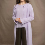 a woman wears  a 100% pure cashmere tee sweater and long cardigan coat in light purple by Irish brand Madigan Cashmere and silk trousers in dark green