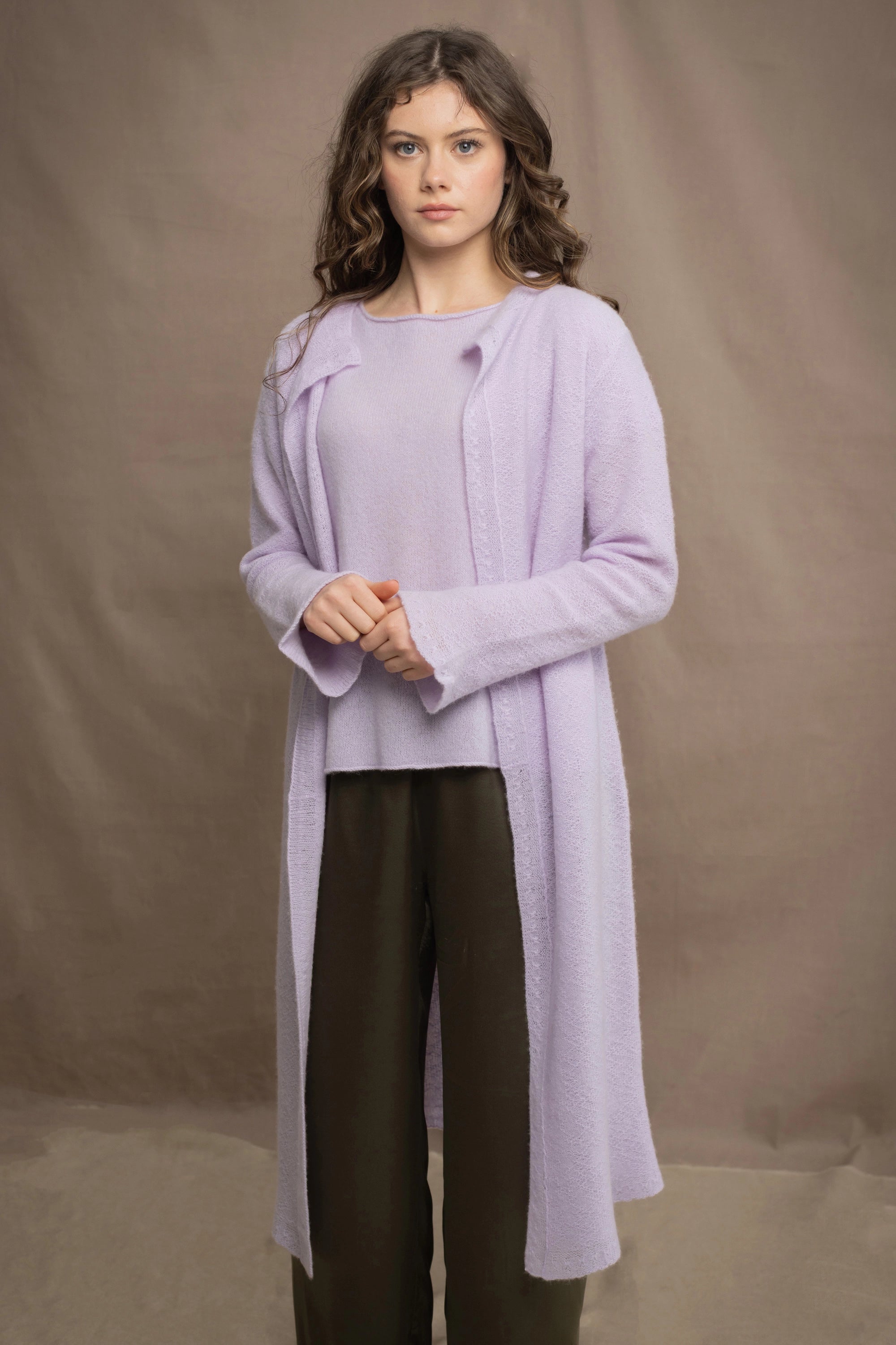 a woman wears  a 100% pure cashmere tee sweater and long cardigan coat in light purple by Irish brand Madigan Cashmere and silk trousers in dark green