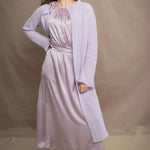Woman wears a light purple cashmere cardigan coat over a matching silk dress by Irish brand Madigan
